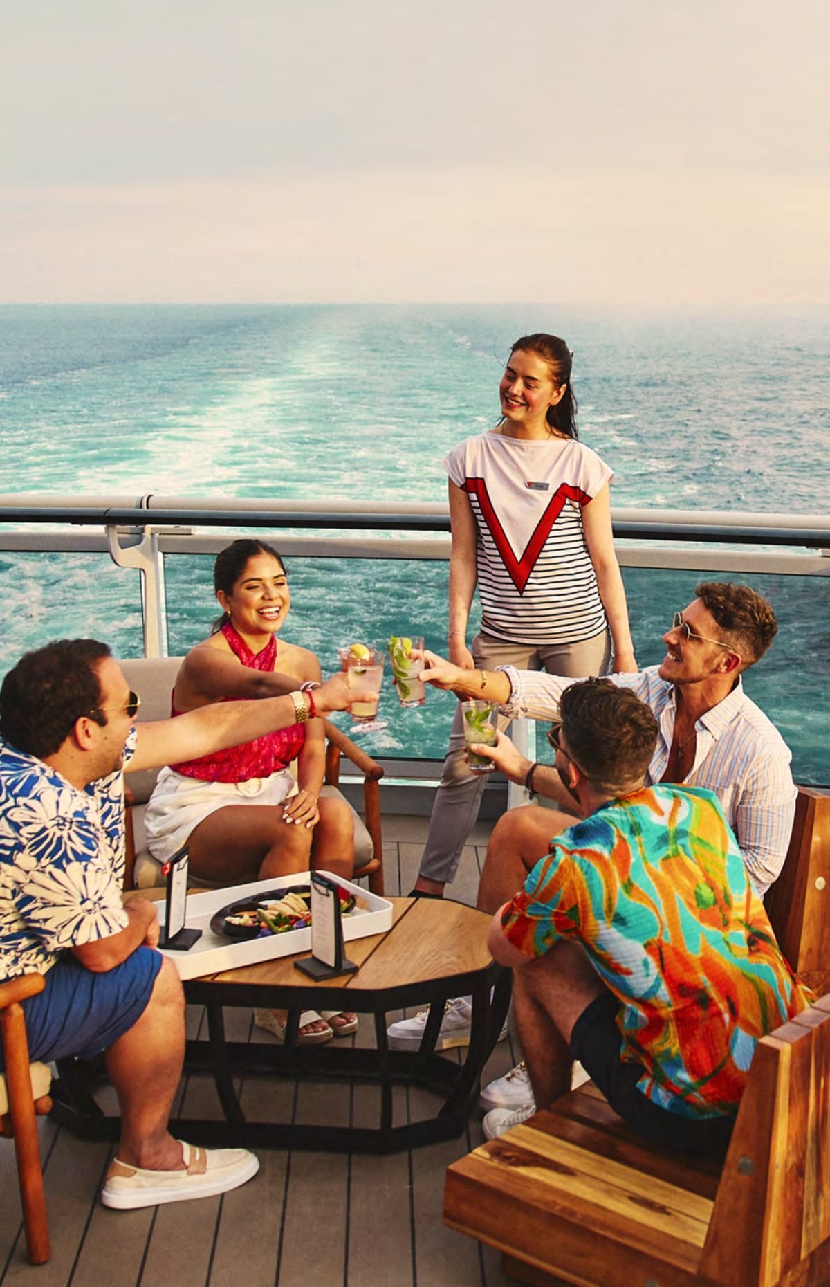 Friends toasting on the aft deck of a Virgin Voyages ship at sunset